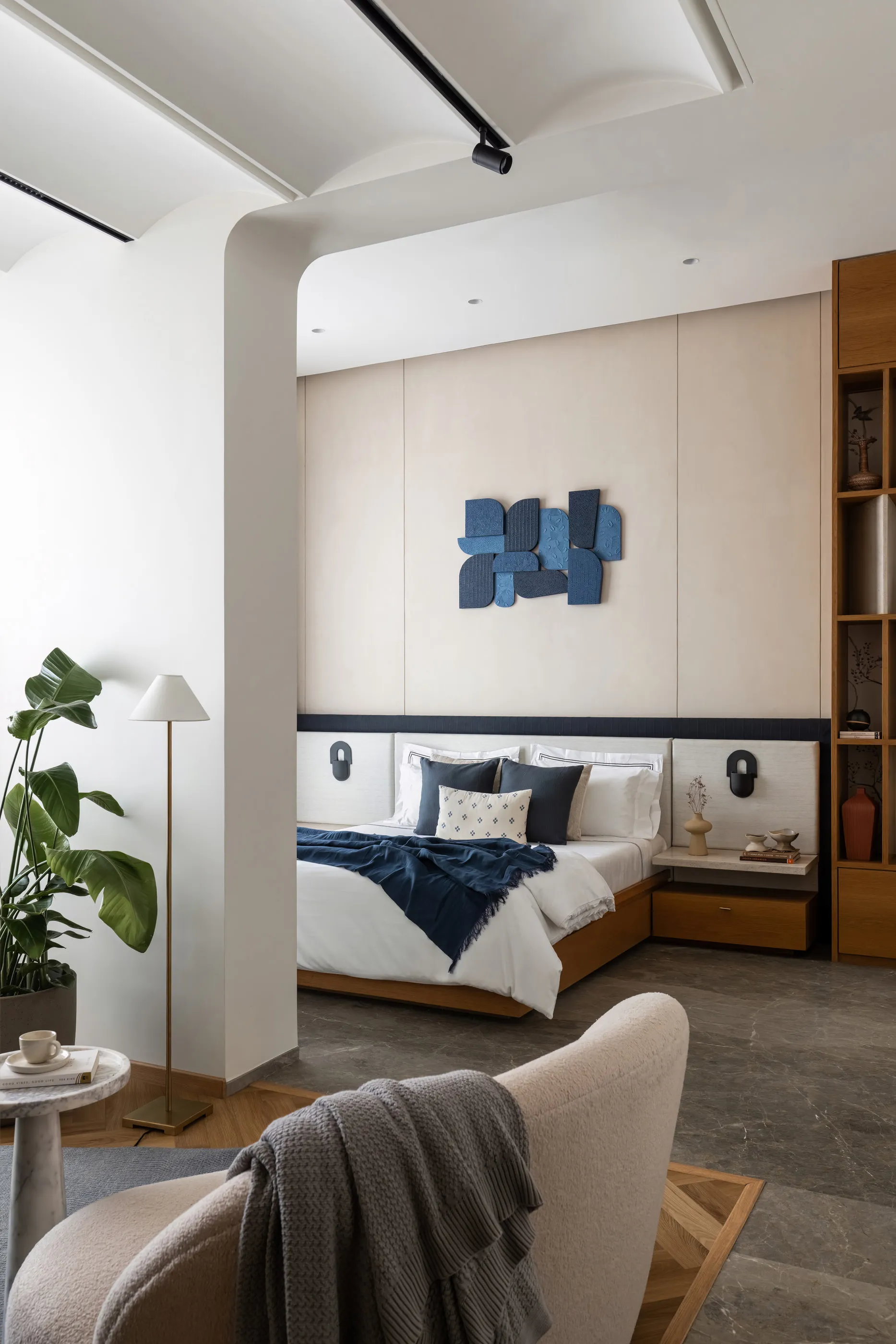 Bedroom framed by a white arch, with a blue wall relief, navy throw and oak bedside shelving